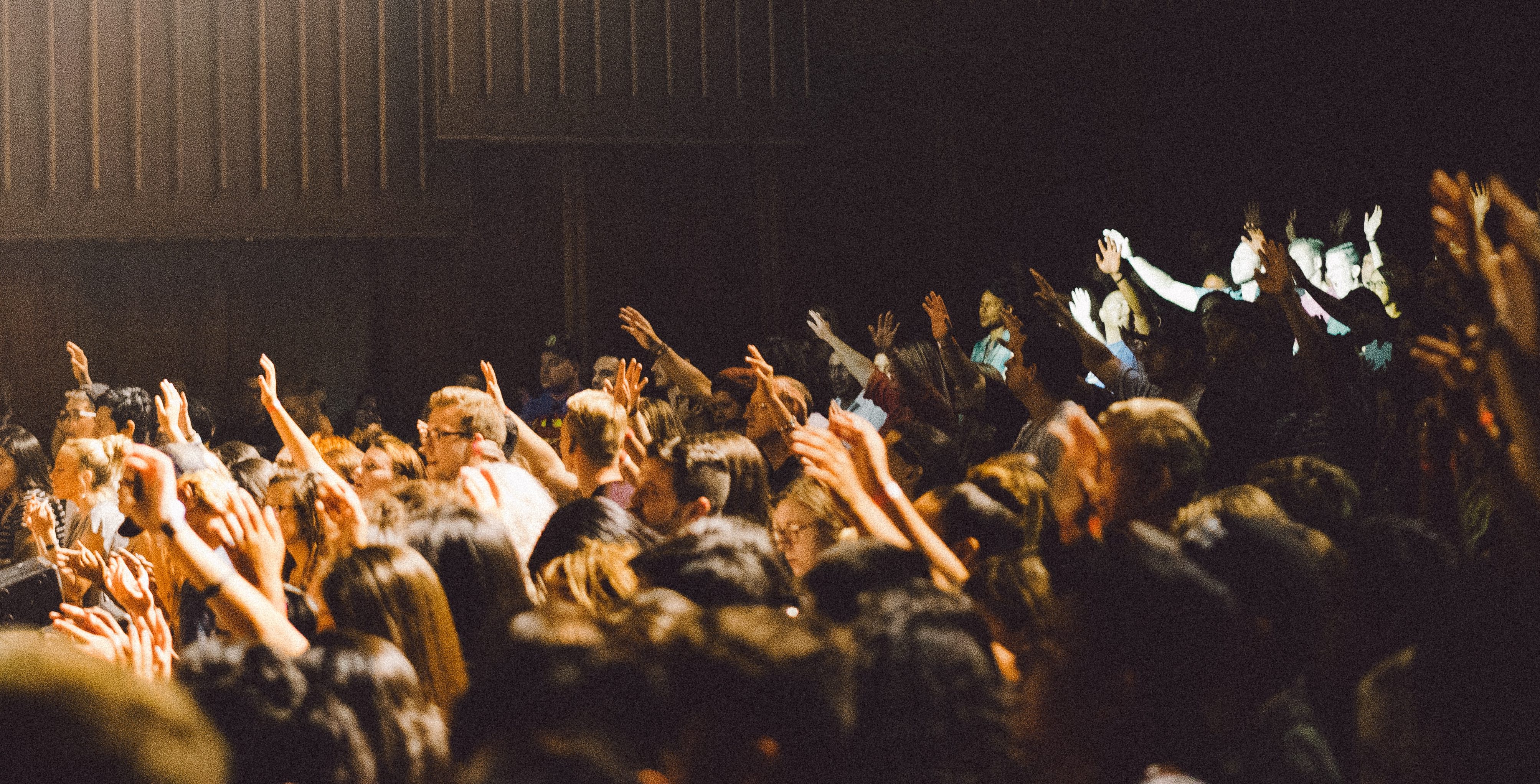 people in the audience of a conference room raising hands