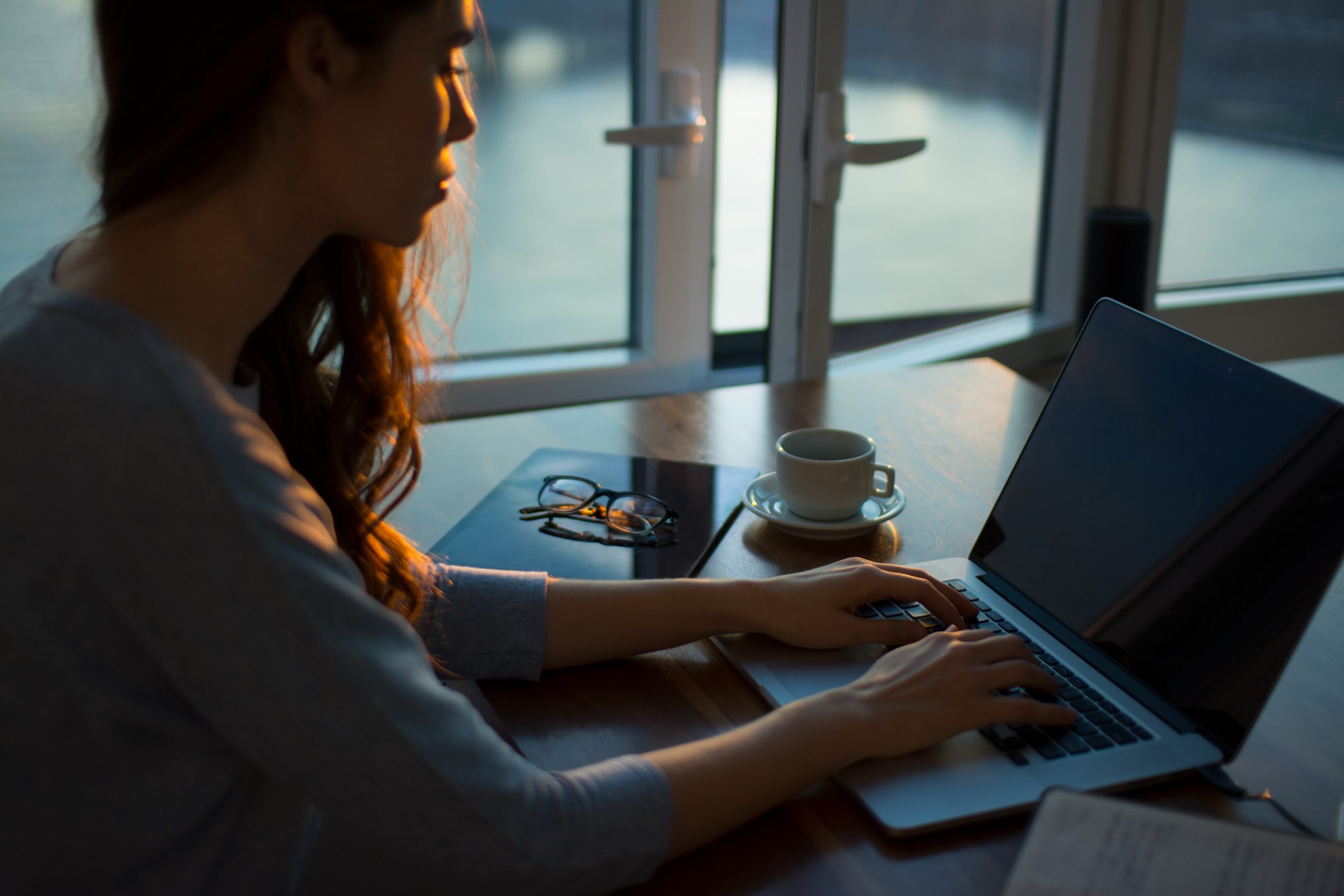 woman working on a laptop, she is sitting by a window that is slightly open