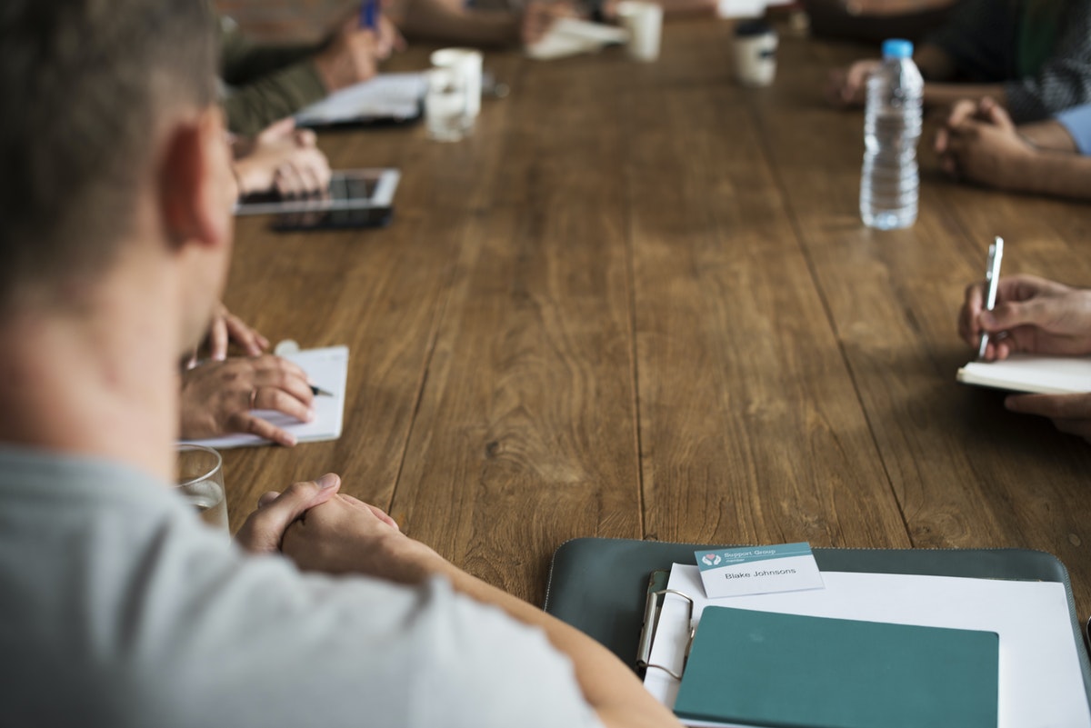 people sitting around a large table, having a meeting. There are notebooks and water glasses over the table