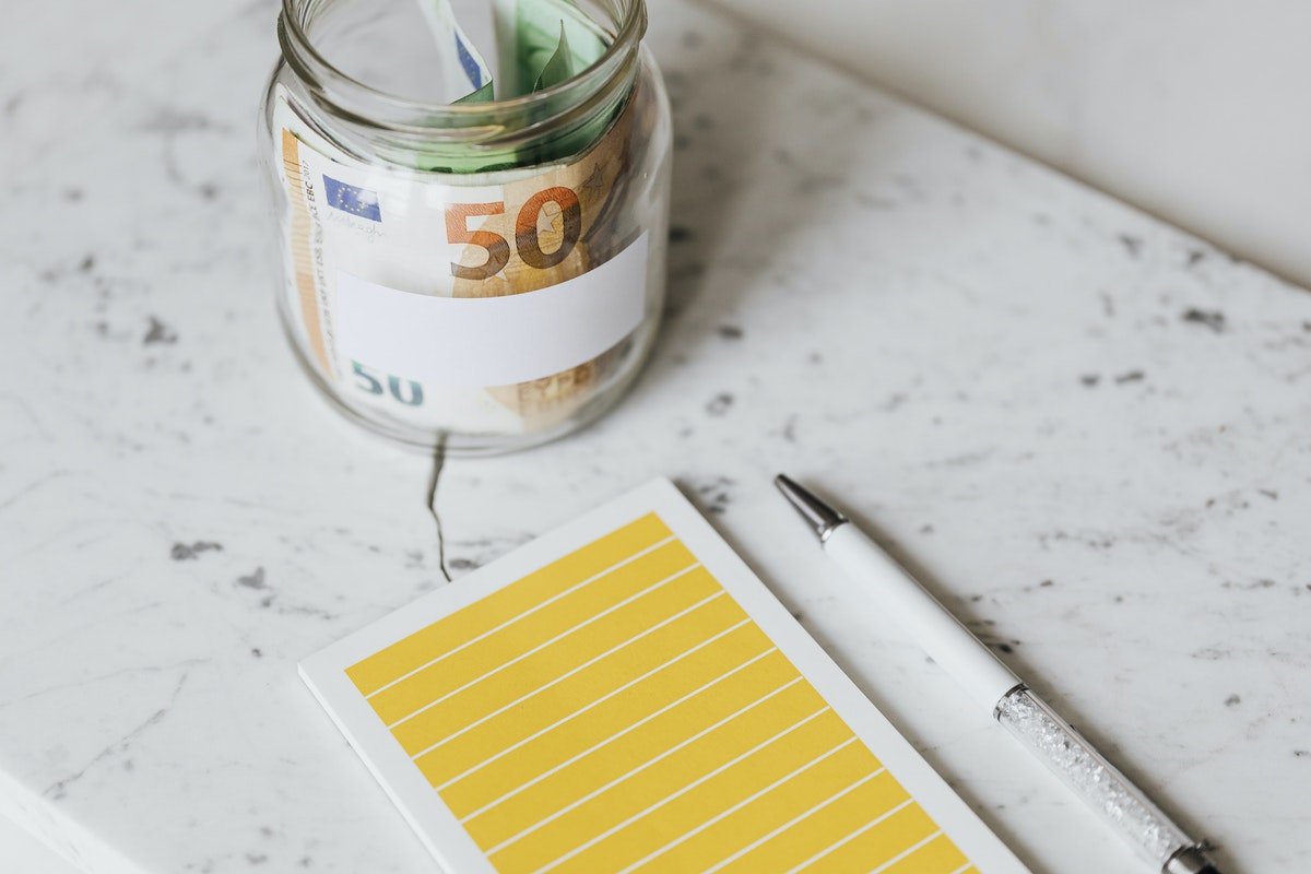 a glass jar with cash in it, near a blank notepad and a pen