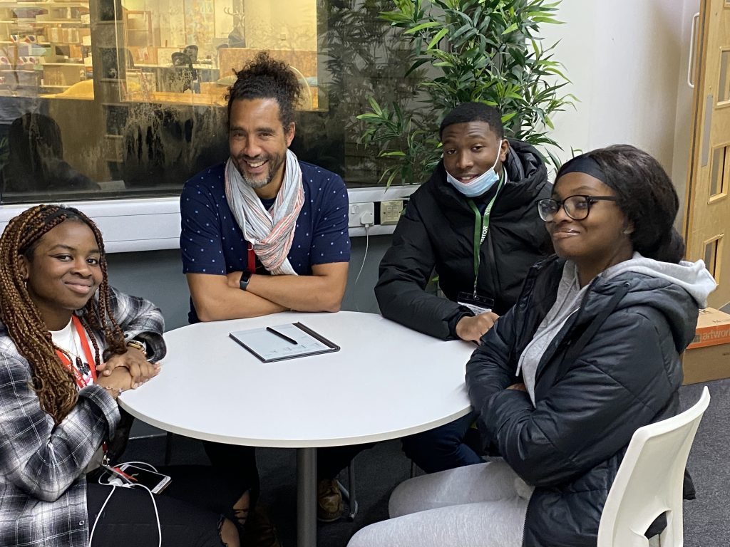 four people sitting around a table, they are all looking at the camera and smiling