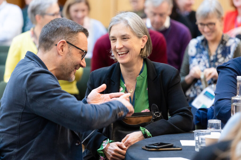 A photograph of a man and a woman in conversation, they are smiling at each other