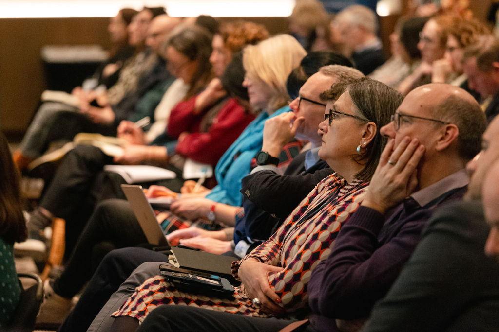 A photo of a row of people sat looking up and listening
