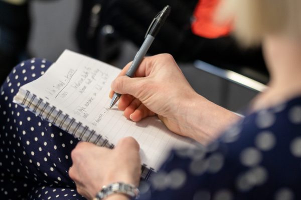 A close up photograph of woman writing in a pad with a pen