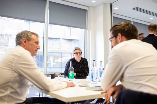 A woman and two men are sat around a table in conversation