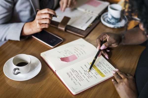 photo of two people having a meeting. they are looking at a notebook and having coffee